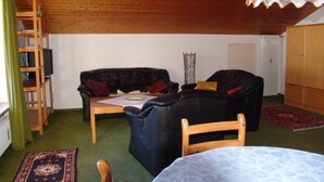 Una sala de estar acogedora con techo de madera, un sofá de cuero negro, una mesa de madera y una alfombra estampada.