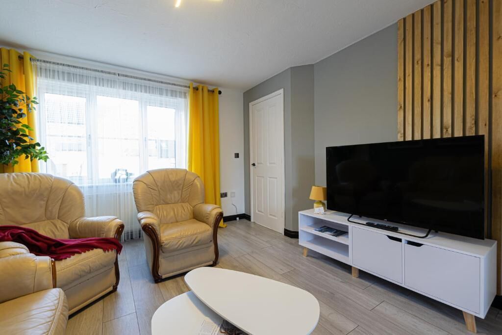 Ein modernes Wohnzimmer mit zwei Ledersofas, einem weißen Couchtisch, einem Flachbildfernseher auf einem weißen TV-Möbel und einer Holzvertäfelung.