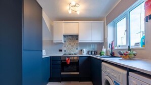 A compact kitchen with a built-in oven, a washing machine, and a window with a view. - Windy House (Sheffield)