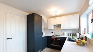 A compact kitchen with white cabinets, a black refrigerator, a tiled backsplash, and a countertop with a fruit bowl. - Windy House (Sheffield)