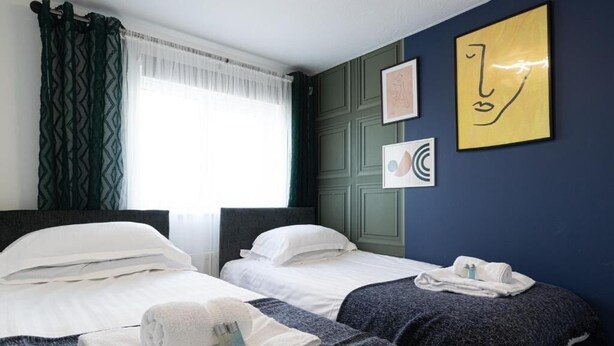 A hotel room with two beds, a window with sheer curtains, and artwork on the walls. - Windy House (Sheffield)