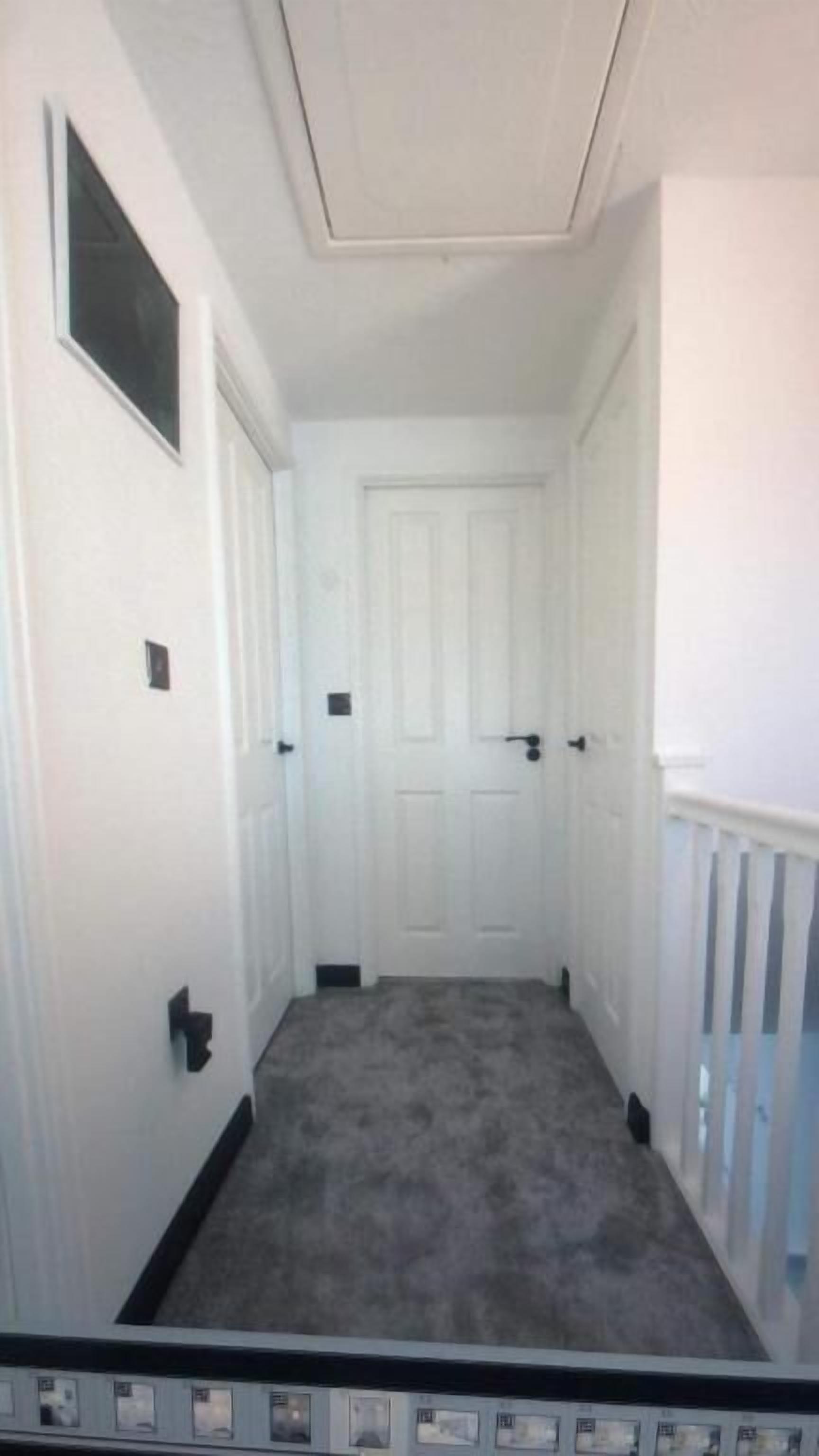 A narrow hallway with white walls, a grey carpet, and a white door at the end.