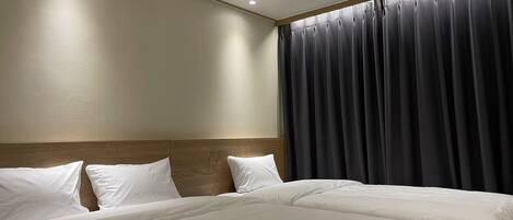 A hotel room with two beds, a wooden headboard, and a large window with dark curtains.