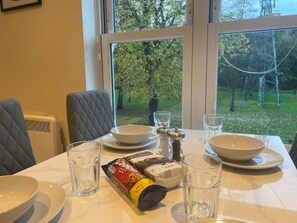 A dining table with white plates, bowls, and glasses, a packet of snacks, and a salt shaker. - Luxurious 1 bedroom flat with free parking (Woking)