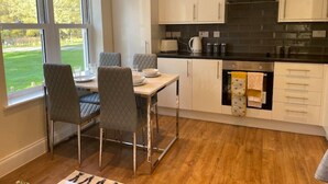 Une cuisine moderne avec des meubles blancs, un plan de travail noir et une vue sur un paysage verdoyant grâce à de grandes fenêtres.