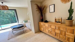 Una sala de estar moderna con un gran ventanal, un mueble de madera, una lámpara de pie y una planta en maceta.