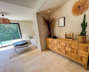 A modern living room with a large window, a wooden cabinet, a floor lamp, and a potted plant.