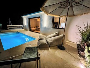 Un espace piscine extérieur moderne, doté d’une chaise longue et d’un parasol.