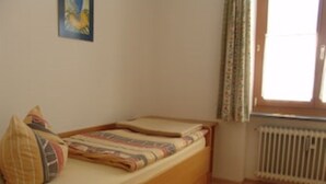 Une petite chambre avec un lit simple, un cadre de lit en bois, un radiateur et une fenêtre avec des rideaux.