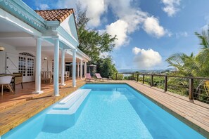 A swimming pool with a wooden deck, white columns, and a view of the sea. - Villa Caluma - Three Bedroom Villa, Sleeps 6 (Les trois ilets)