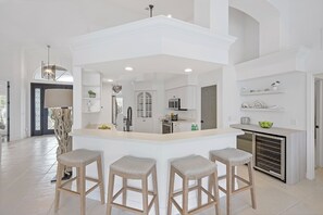 A modern kitchen with a central island, bar stools, and built-in appliances. - Waterfront Oasis | Pool, Kayaks & Steps to Beach (Marco Island)