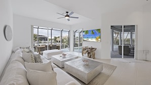 Een moderne woonkamer met een grote bank, twee bijzettafels en uitzicht op een tropisch strand door grote ramen.