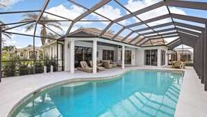 Zwembad met een overdekt terras, palmbomen en een helderblauwe lucht.