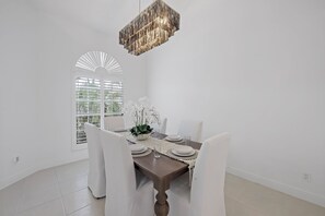A dining area with a wooden table set for four, white chairs, a white table runner, and a hanging light fixture.