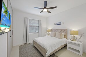 A bedroom with a bed, nightstands, a ceiling fan, a TV, and a window with blinds. - Waterfront Oasis | Pool, Kayaks & Steps to Beach (Marco Island)