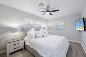 A bedroom with a bed, nightstands, a ceiling fan, and two windows with blinds.