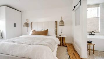 A modern bedroom with a large bed, bedside tables, a hanging light fixture, and a view to a bathroom.