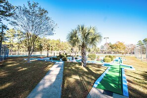 Un parque con un sendero, palmeras y una zona de césped artificial verde.