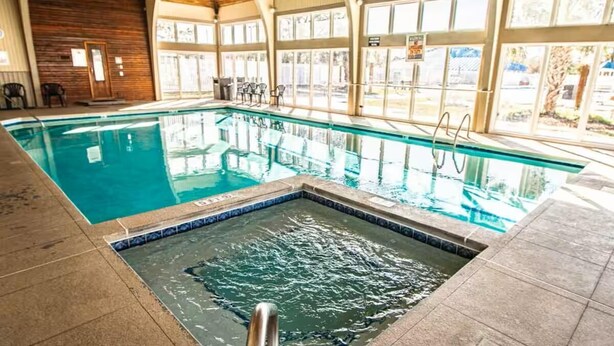 Una piscina interna con acqua cristallina, un trampolino e una zona solarium piastrellata.