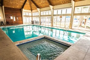 An indoor swimming pool with clear water, a diving board, and a tiled deck area. - Waterwood Townhome (New Bern)