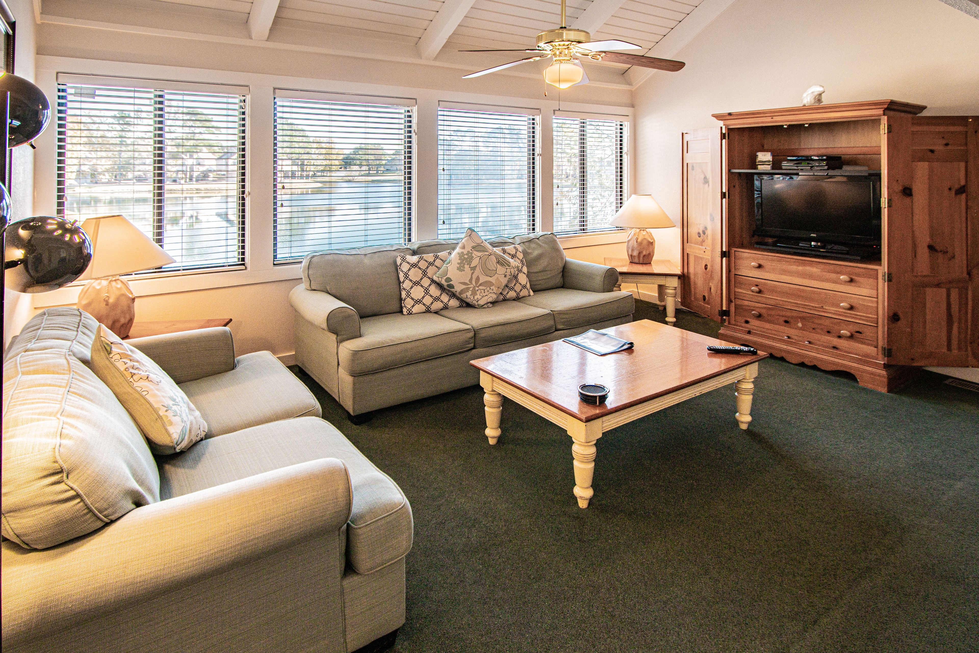 A living room with a sofa, a coffee table, a TV cabinet, and a ceiling fan.