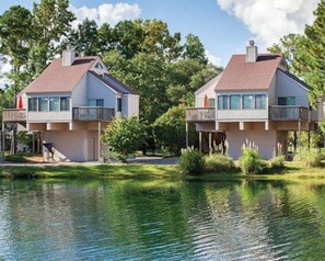 Dos casas frente al agua con balcones, un área con césped y una masa de agua.