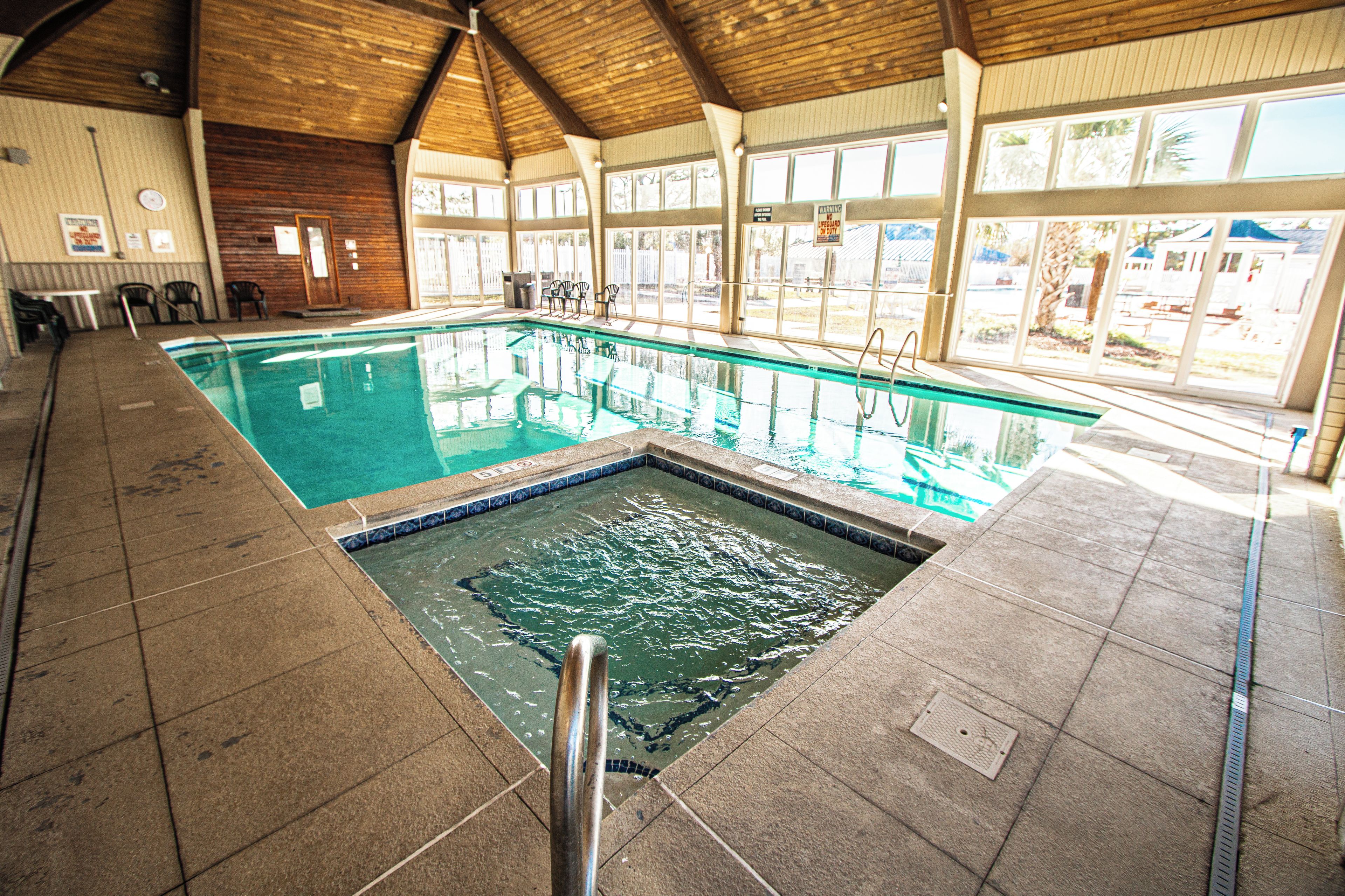 Una piscina interior con suelo de baldosas, un trampolín y techo de madera.