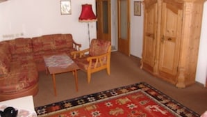 Ein Wohnzimmer mit einer Couch, einem Sessel, einem kleinen Tisch, einem Holzschrank und einem gemusterten Teppich.
