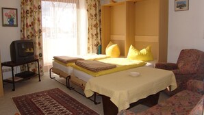 Een slaapkamer met een bed, een stoel, een televisie op een dressoir en een raam met gordijnen.