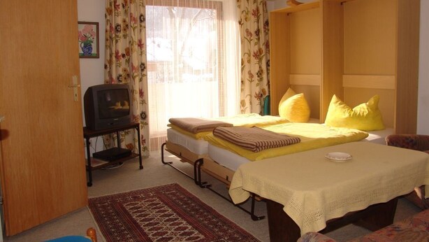 Een slaapkamer met een bed, een televisie, een houten garderobe en een raam met bloemen gordijnen.