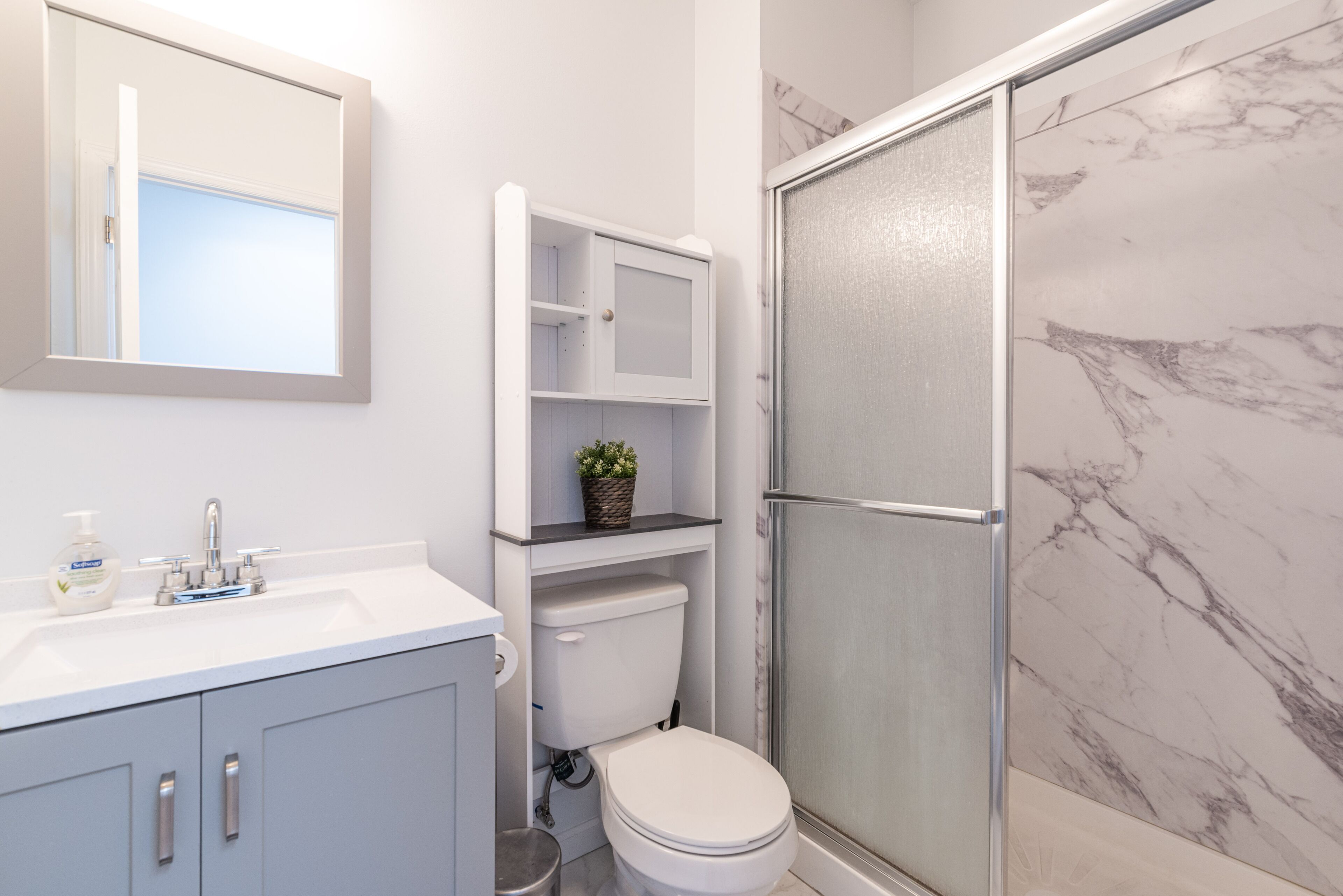 A bathroom with a white sink, a toilet, a shower with a glass door, and a marble wall.