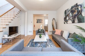 A modern living room with a staircase, a flat-screen TV, a coffee table, and a large abstract painting. - Zen Private House for Family 4 BR 3 BA (Jersey City)