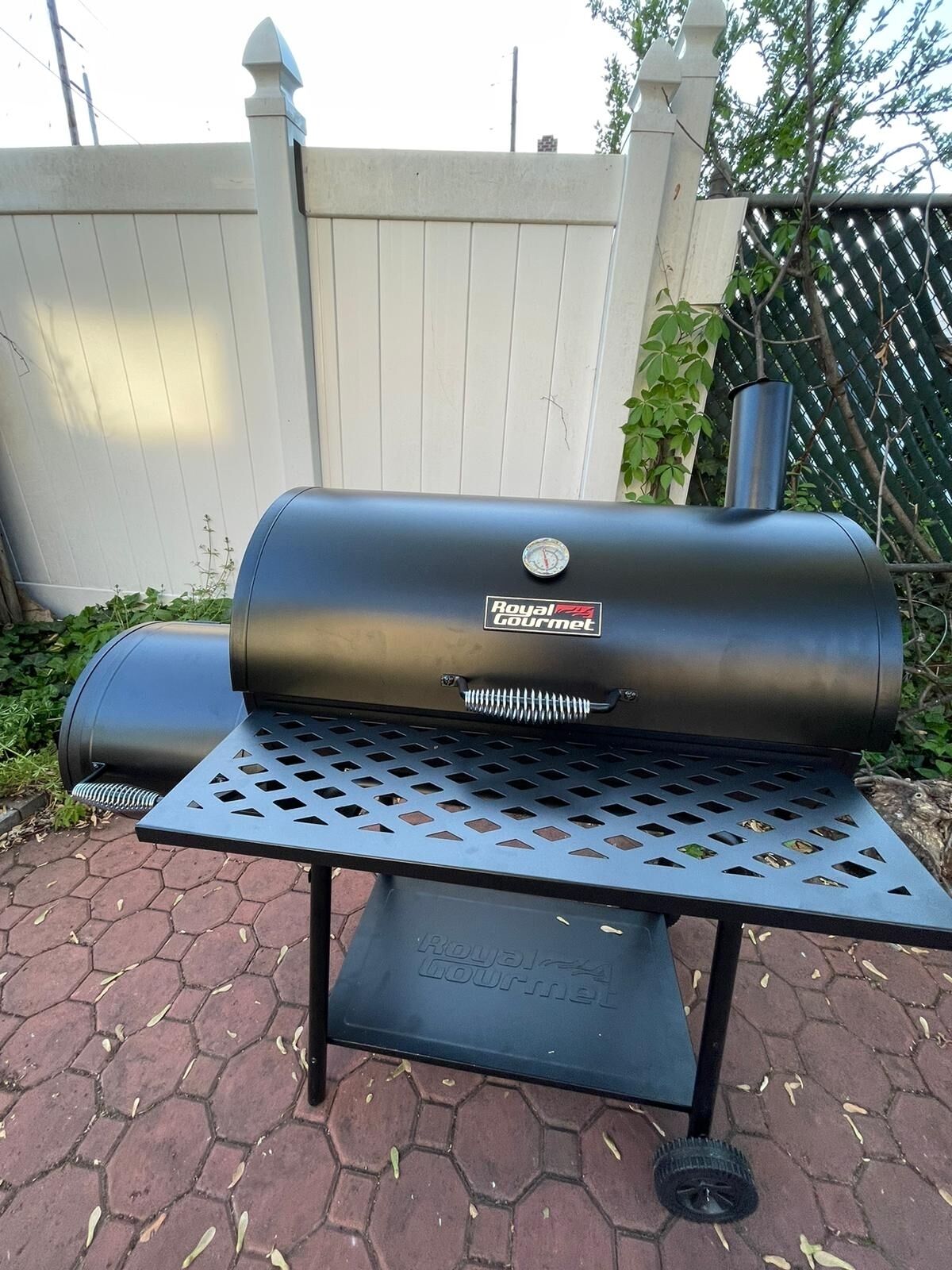 Una parrilla portátil para barbacoa con termómetro digital, ubicada sobre un soporte metálico con suelo de baldosas hexagonales.