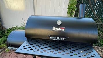 Una parrilla portátil para barbacoa con termómetro digital, ubicada sobre un soporte metálico con suelo de baldosas hexagonales.