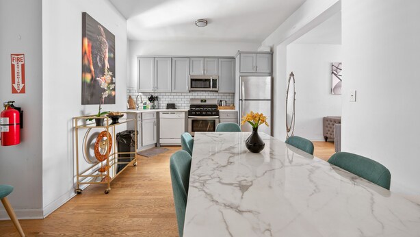 A modern kitchen with white cabinets, a marble island, and teal chairs.