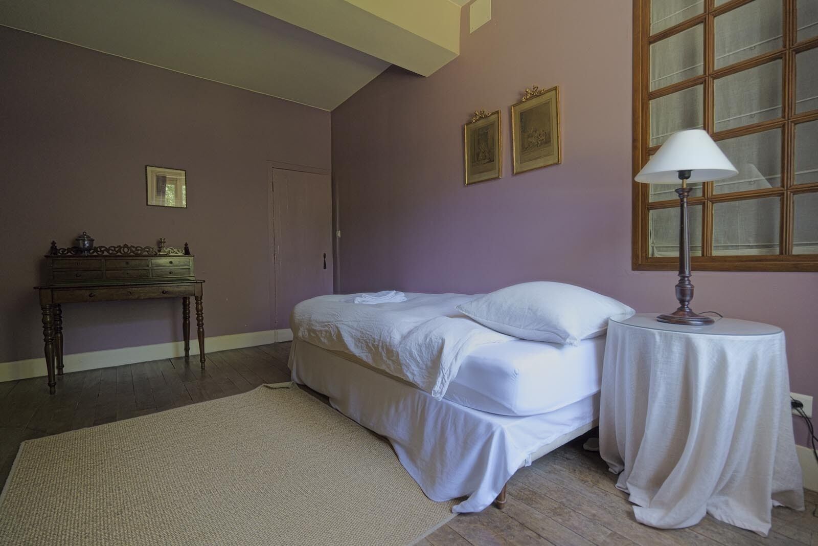 Un dormitorio con cama, mesita de noche, cómoda y dos cuadros en la pared.