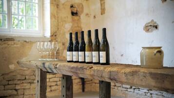 Uma mesa de madeira rústica com garrafas de vinho e copos numa sala com paredes de pedra e uma janela.