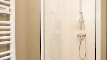 Ducha a pie con puerta de vidrio, suelo de madera y un toallero blanco.