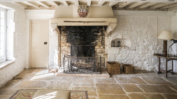 Una chimenea de piedra con repisa blanca, una puerta de madera y una ventana a la izquierda.