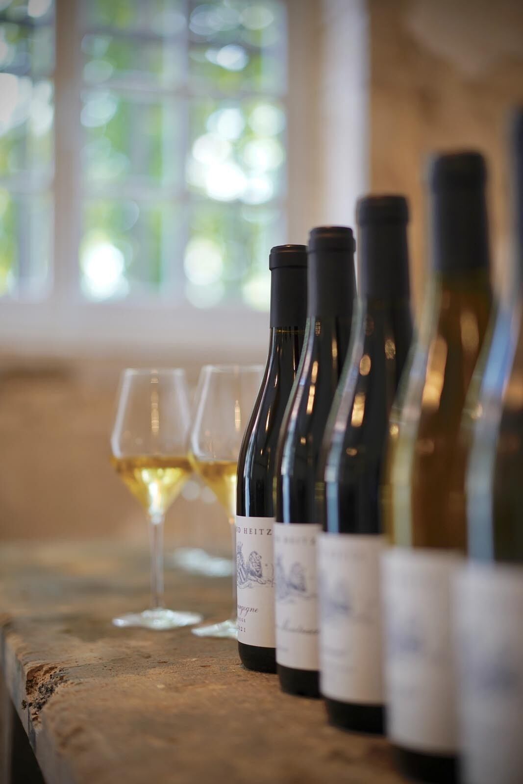 A row of wine bottles on a wooden counter with a glass of white wine.