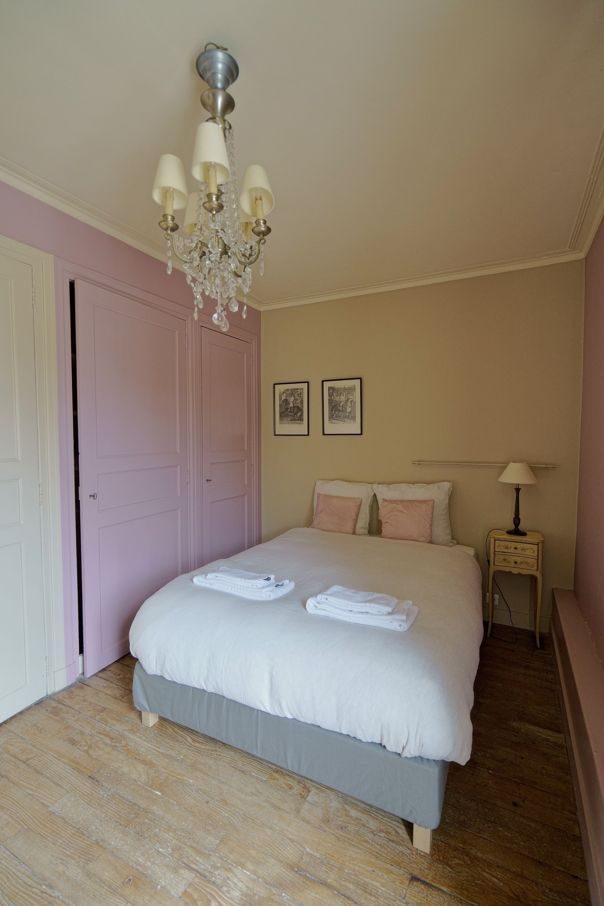 Een slaapkamer met een bed, een kroonluchter, een nachtkastje en een deur.