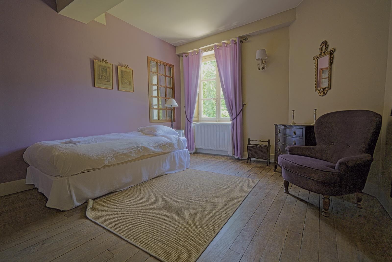 Een slaapkamer met een bed, een stoel, een dressoir en een raam met gordijnen.