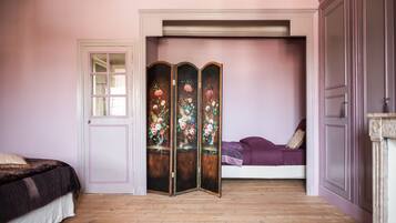 A bedroom with a bed, a door, a wooden floor, and a wall-mounted decorative panel.