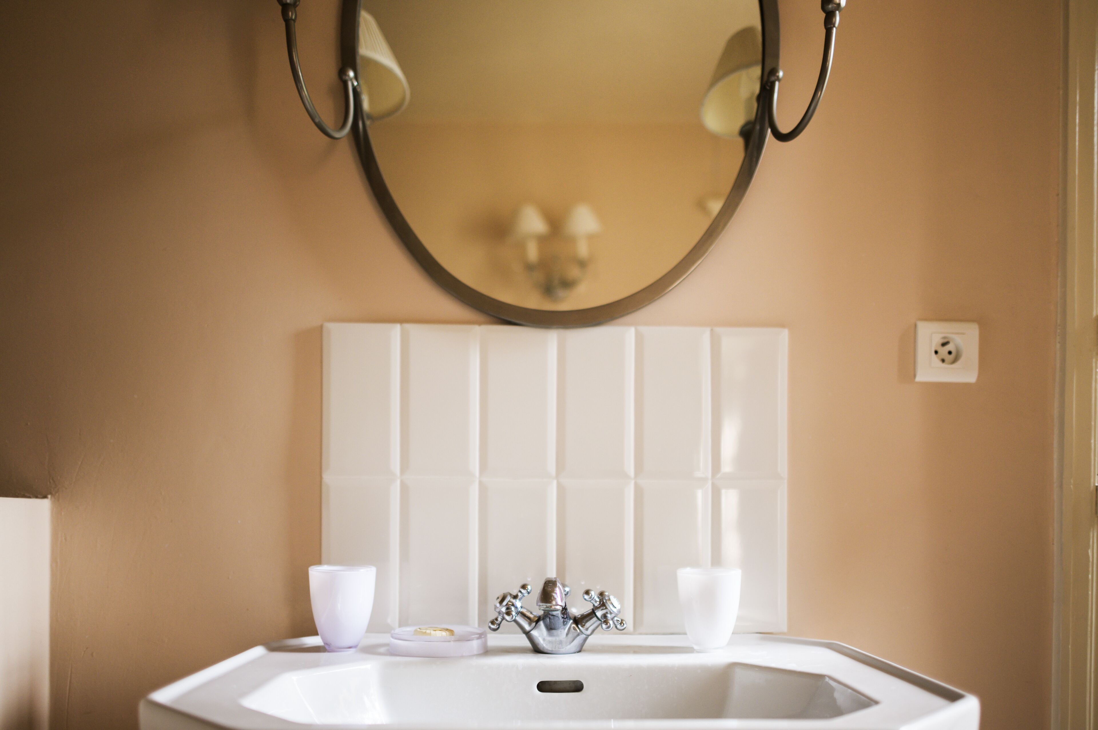 Een badkamer met een witte wastafel, een spiegel en een beige wand.