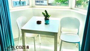 A corner room with a table and two chairs, a potted plant, and a view of a building with a sign reading "LOGISTICS". - Cozi 8 Apartment (Thành phố Hồ Chí Minh)