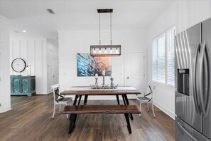 A modern kitchen with a wooden table, white chairs, a stainless steel refrigerator, and a pendant light. - Sundance: Sleeps 18! 1 Block to Beach! Pool & spa! (Destin)
