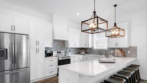 A modern kitchen with white cabinetry, stainless steel appliances, and a central island with bar stools.