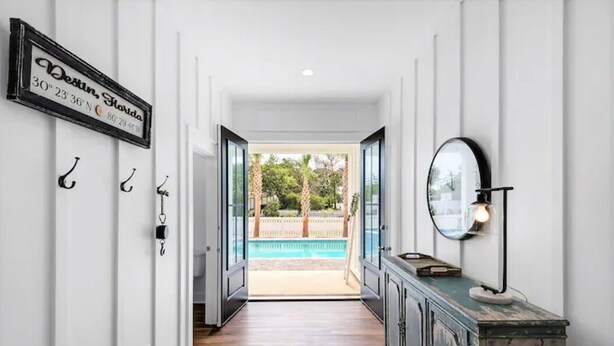 A hallway leading to a pool area with a sign on the wall, a cabinet with a lamp, and a view of the pool.
