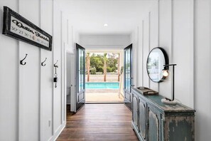 A hallway leading to a pool area with a sign on the wall, a cabinet with a lamp, and a view of the pool. - Sundance: Sleeps 18! 1 Block to Beach! Pool & spa! (Destin)