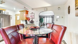 Un coin repas avec une table en verre et des chaises en cuir rouge, une cuisine équipée d’appareils électroménagers modernes et un salon avec un canapé et une plante.
